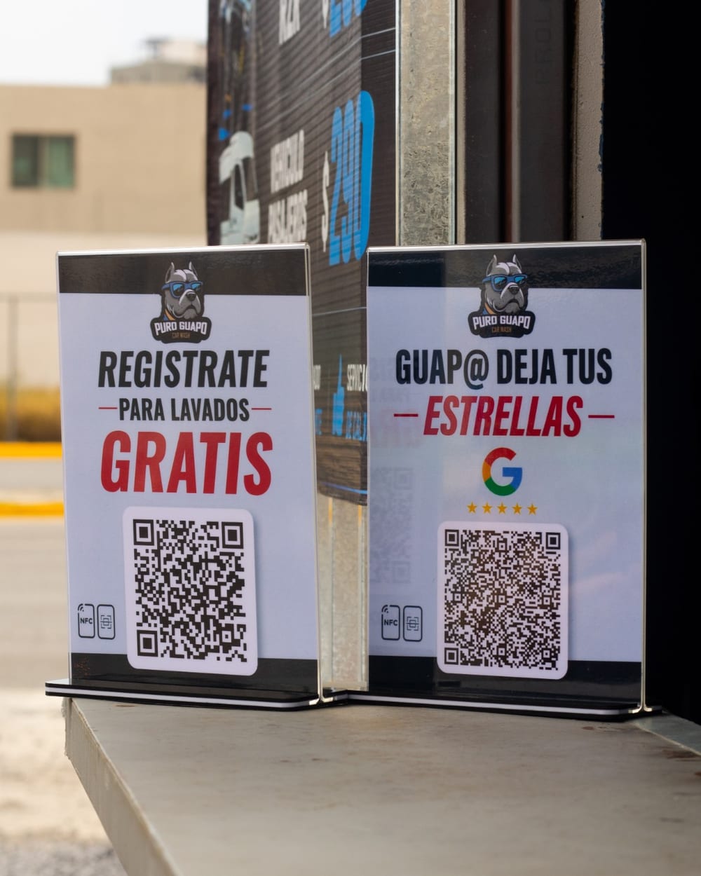 Dos tótems de acrílico de Puro Guapo Car Wash en el mostrador: uno invita a registrarse para lavados gratis y otro a dejar reseña en Google, cada uno con su QR